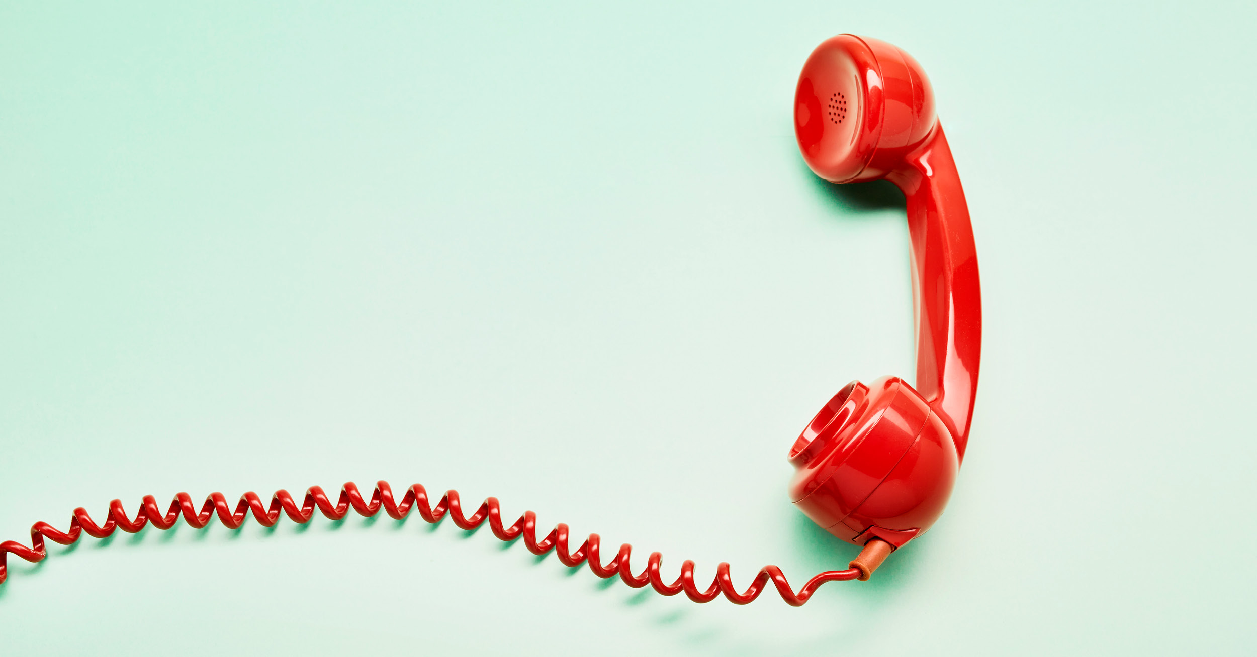 Red mid-century phone receiver on mint background with red coiled wire leading off canvas to the left