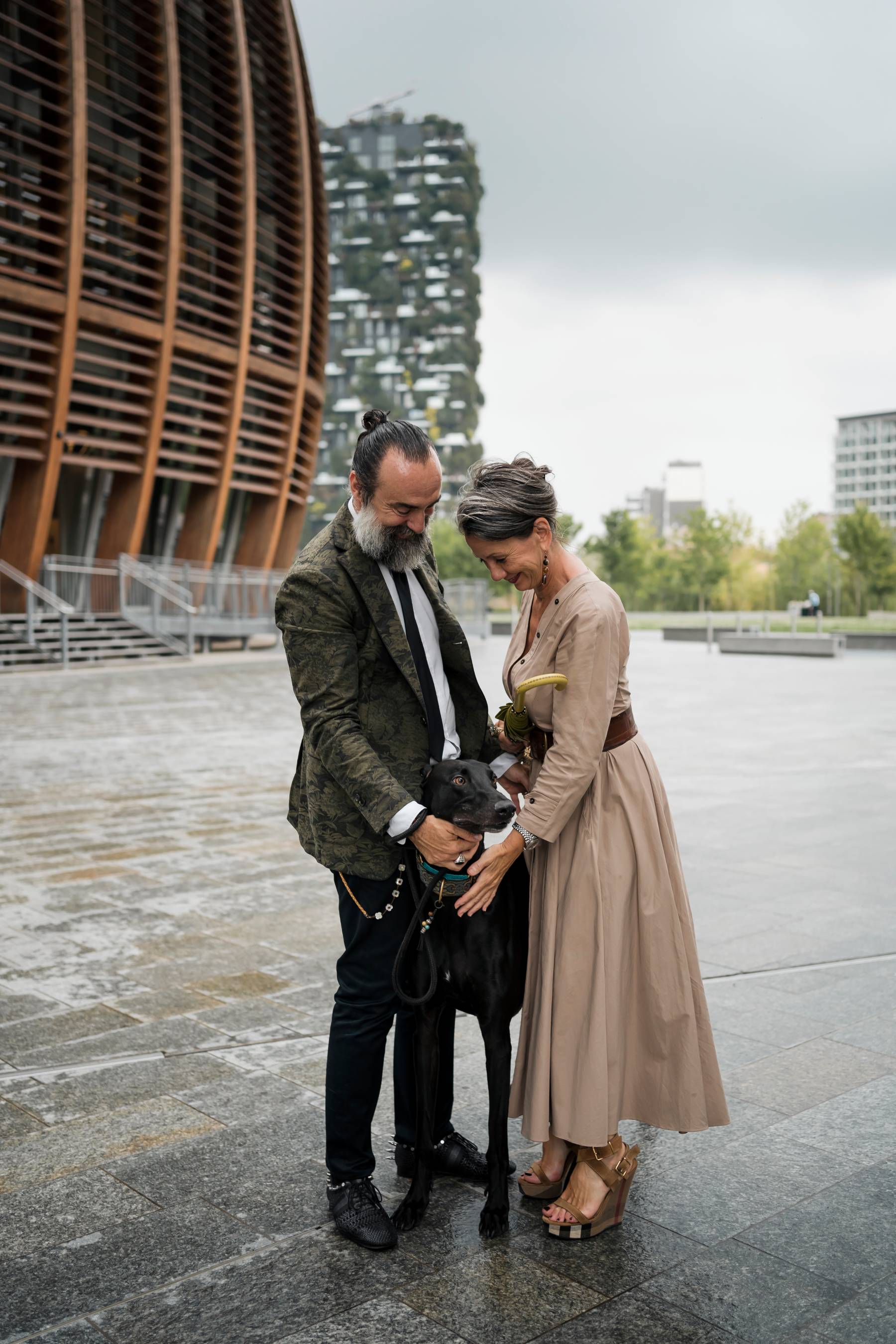 A couple stand together outdoors with their dog on a rainy day
