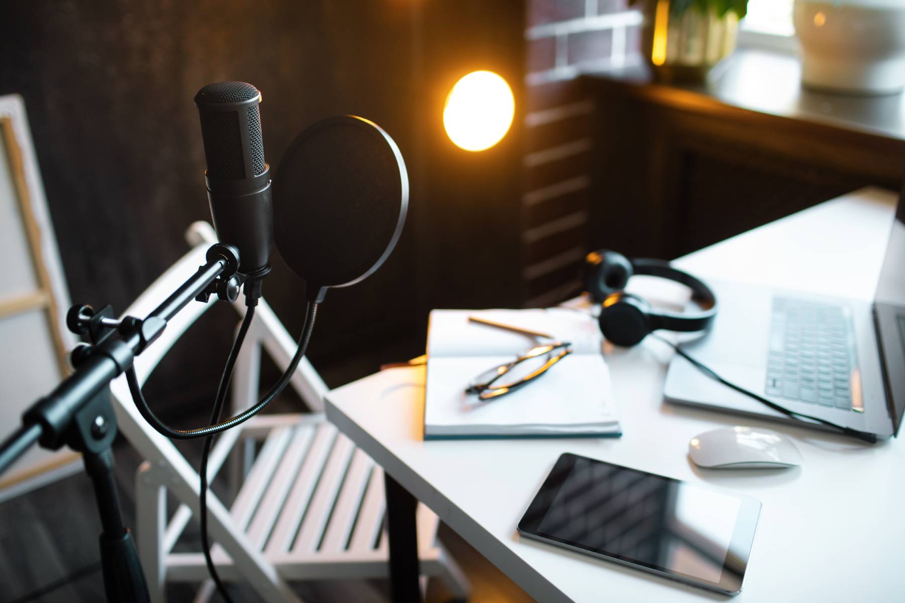 A room set up to record a podcast, with a microphone, and an iPad, headphones and a laptop on a desk