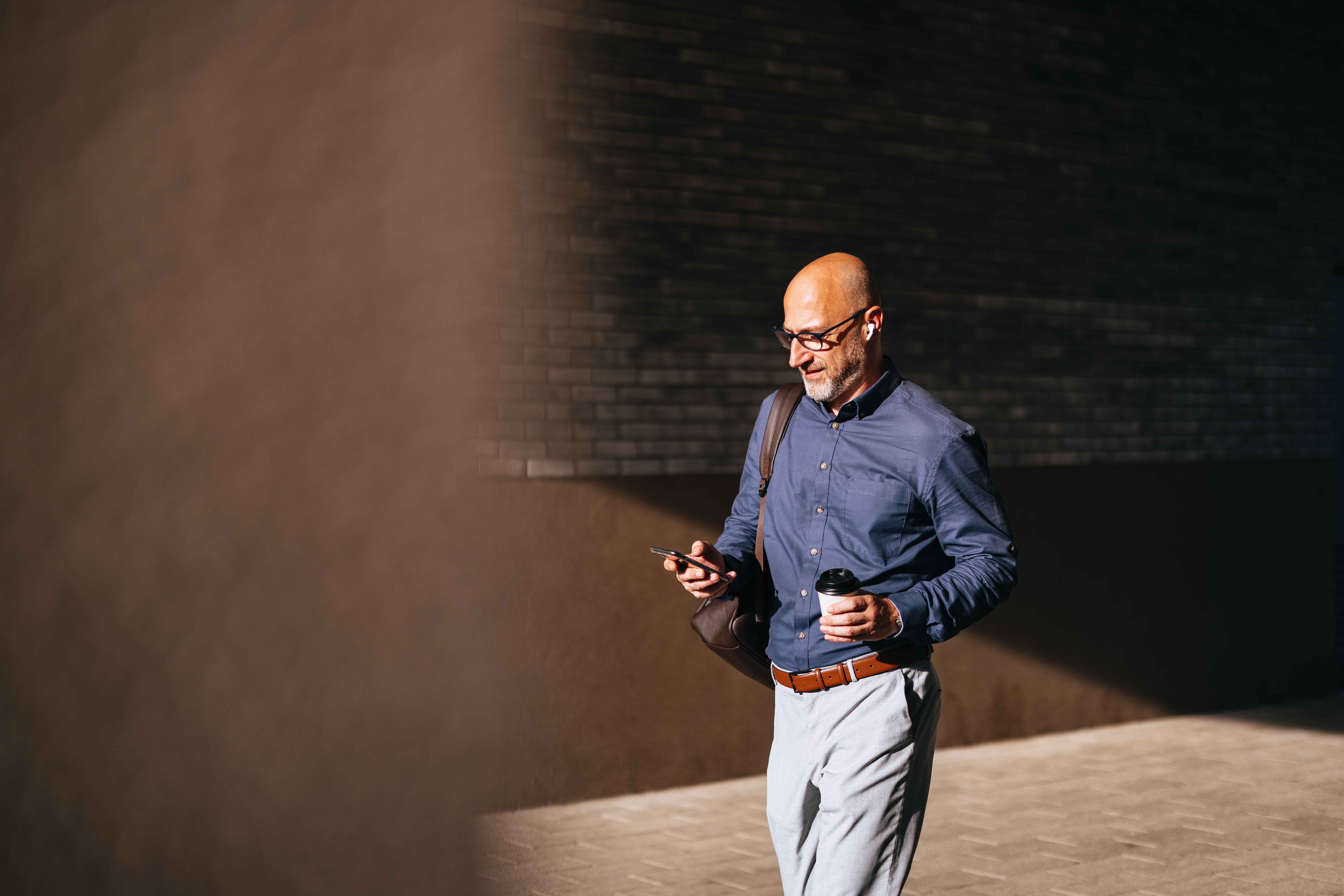 A businessman checks his phone while walking in the sun