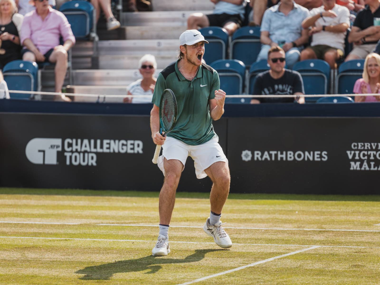 An Ilkley Lawn Tennis Club player on court in front of a Rathbones sign