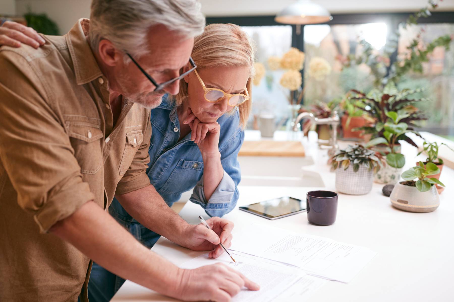 A couple look at paperwork spread out across their kitchen bench together