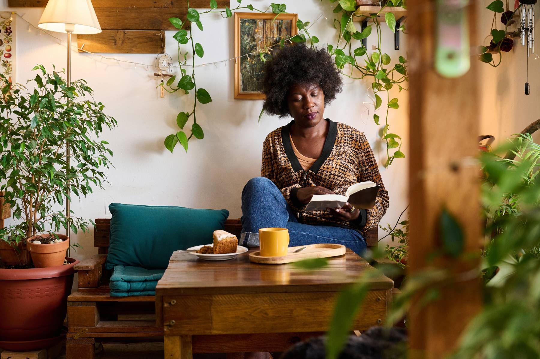 A woman sits in a café reading a book while having a hot drink and cake