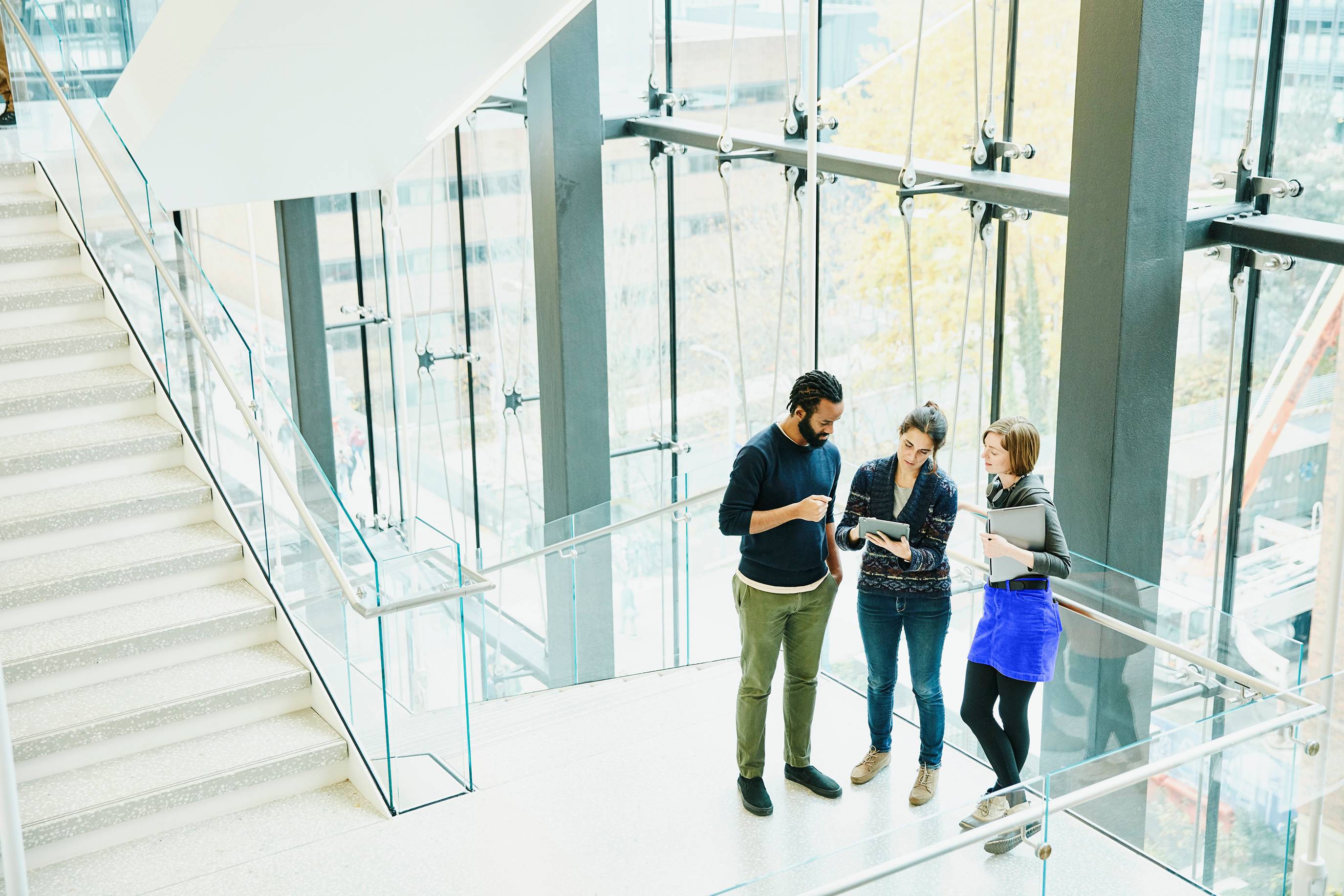 Thee office workers talk on the stairs of a glass corporate office building