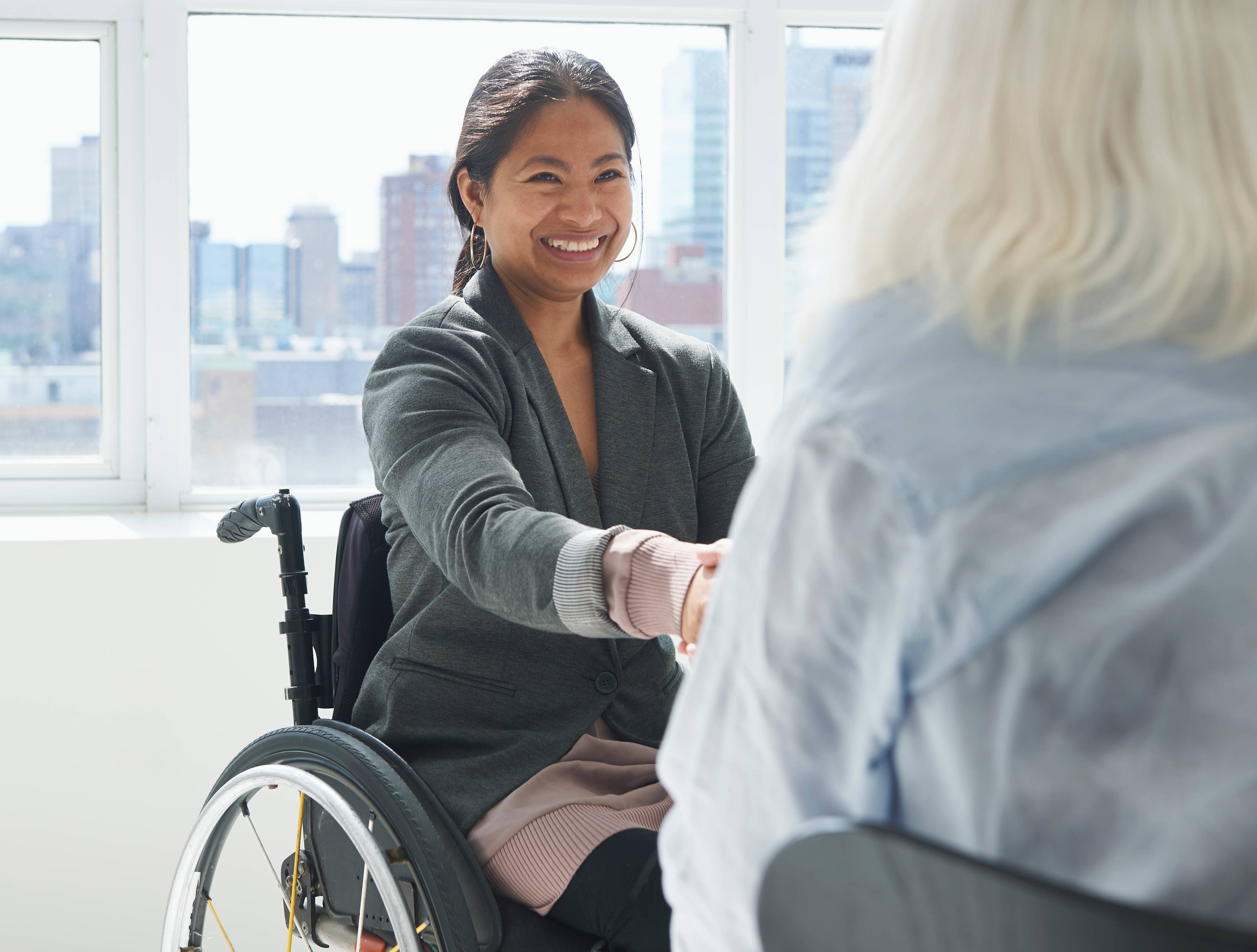 A confident businesswoman with a disability is sitting in a wheelchair and shaking hands with a colleague.