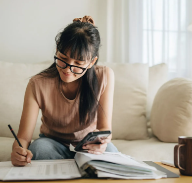 young woman writing in notepad on coffee table wearing glasses