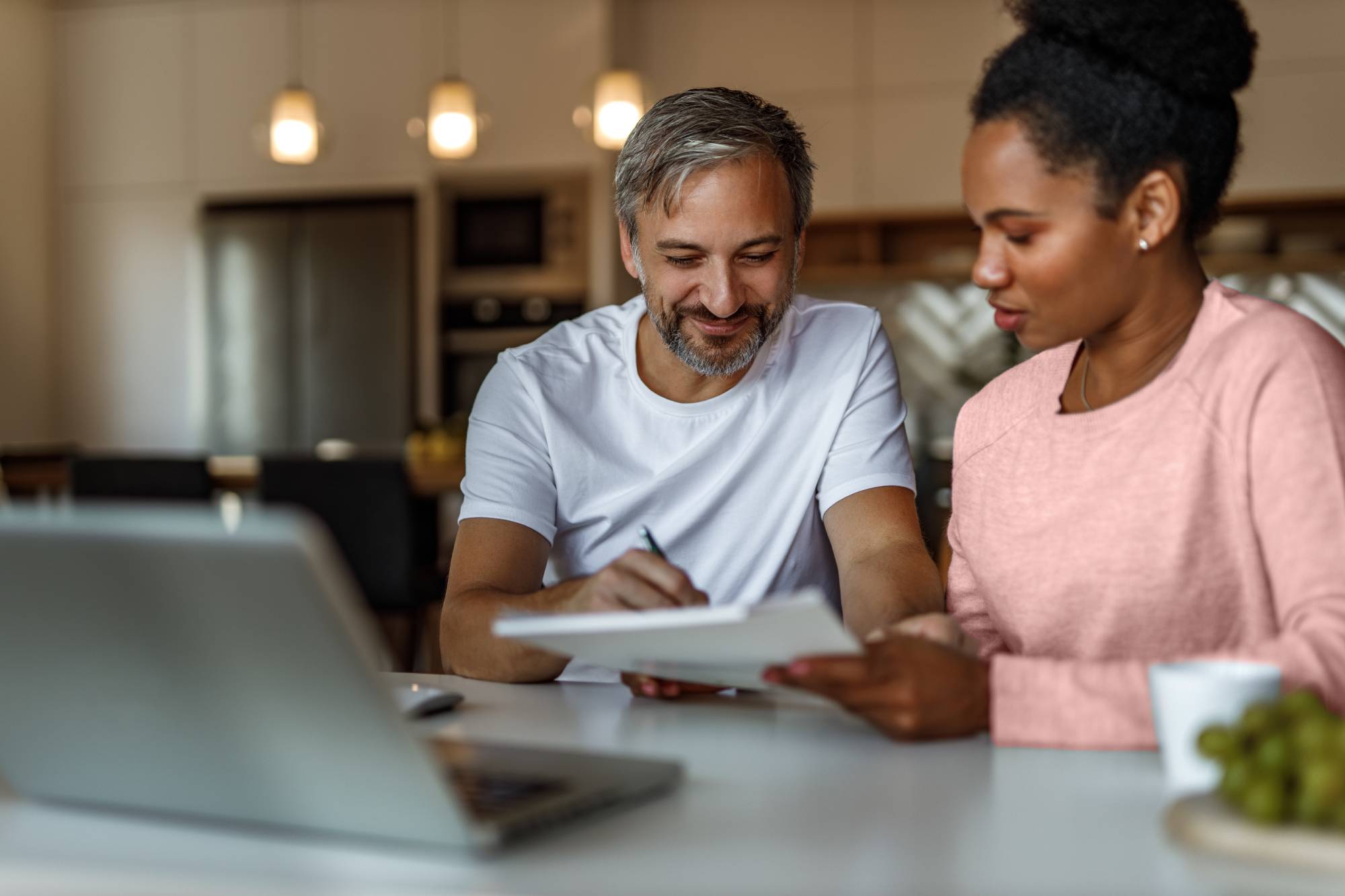 A couple draw on a document in front of a laptop in their home