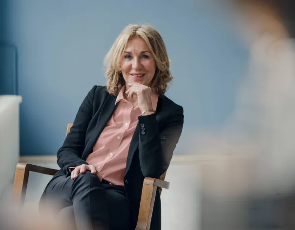 A financial adviser smiles at the camera while sat in a wooden chair
