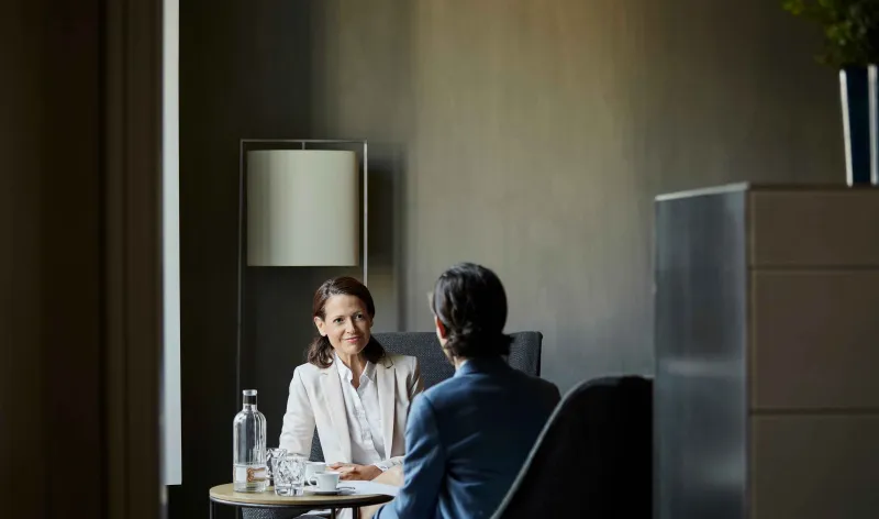 An accountant has coffee with their client in a meeting room