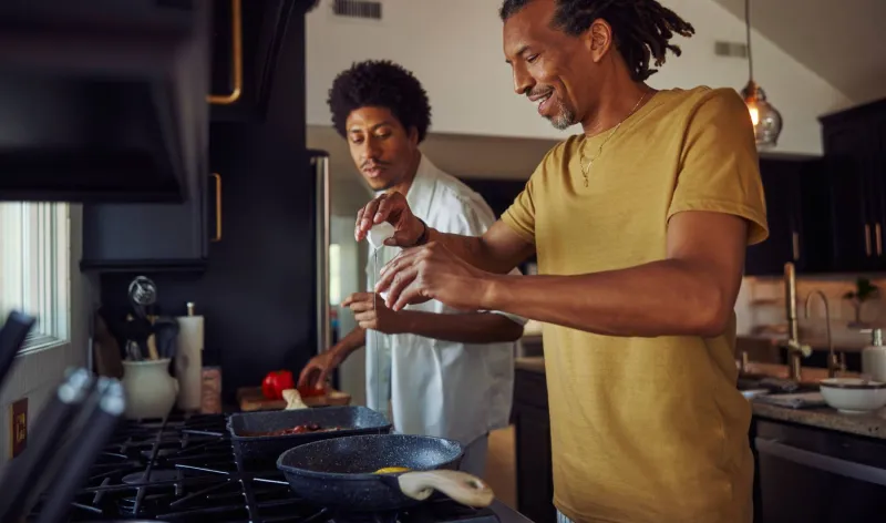 A father and son cook eggs together in the kitchen