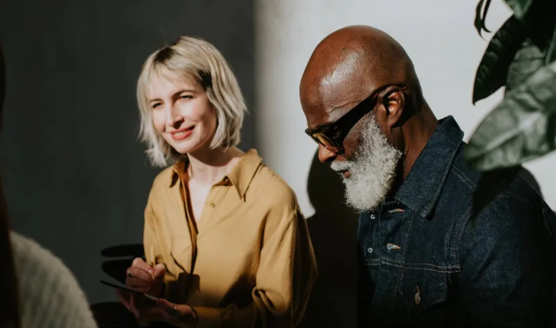 A man and woman study information on a tablet while talking to someone