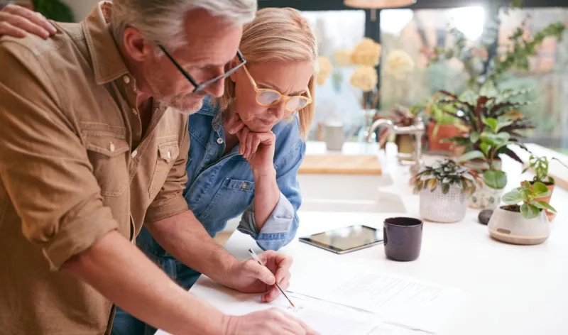 A couple review documents spread out across their kitchen bench together
