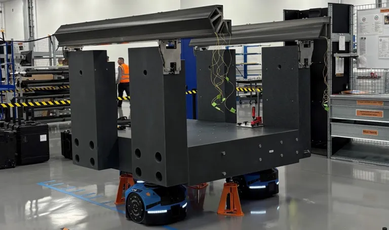 Large industrial machine on wheeled platforms inside a factory floor.