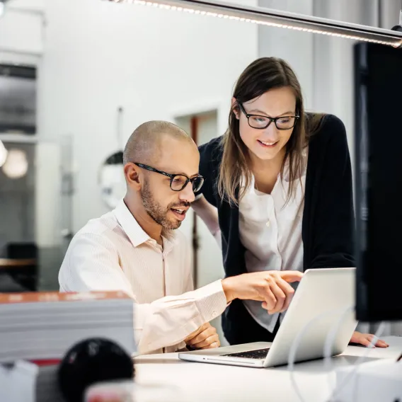 A man ad woman in an office look at a laptop together