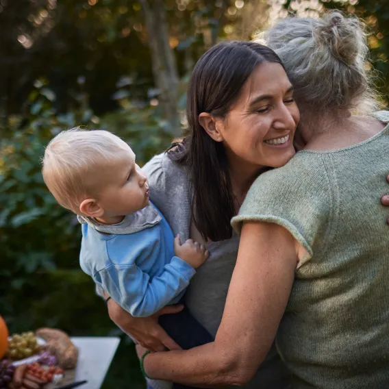 A lady hugs another while holding a baby