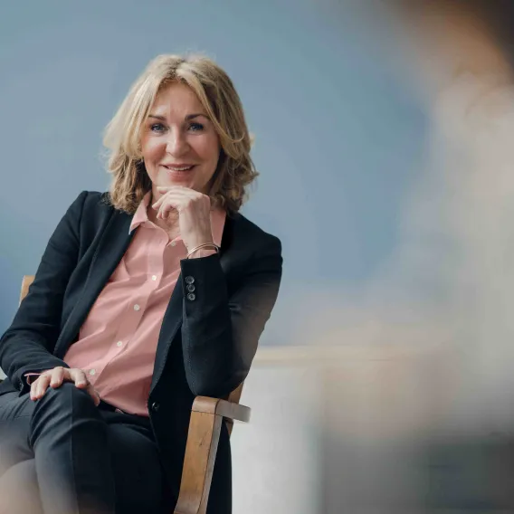 A professional woman looks towards the camera with a curious facial expression while sat in a chair
