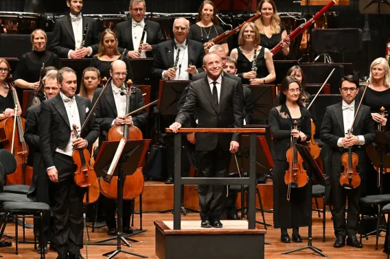 The Bournemouth Symphony Orchestra stands while the audience applauds, with conductor Mark Wigglesworth in front