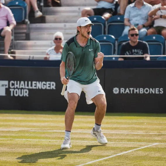 An Ilkley Lawn Tennis Club player on court in front of a Rathbones sign