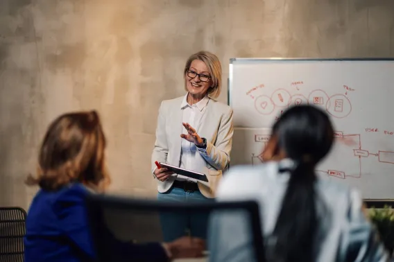 A financial adviser speaks to other advisers while standing by a whiteboard