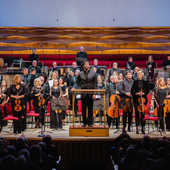 The Royal Liverpool Philharmonic Orchestra stands to applause, with conductor Domingo Hindoyan in front