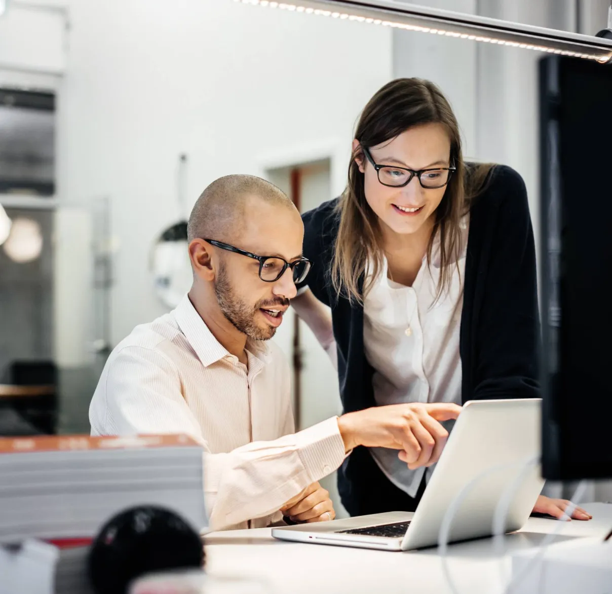 Two work colleagues discuss something on a laptop screen at a desk