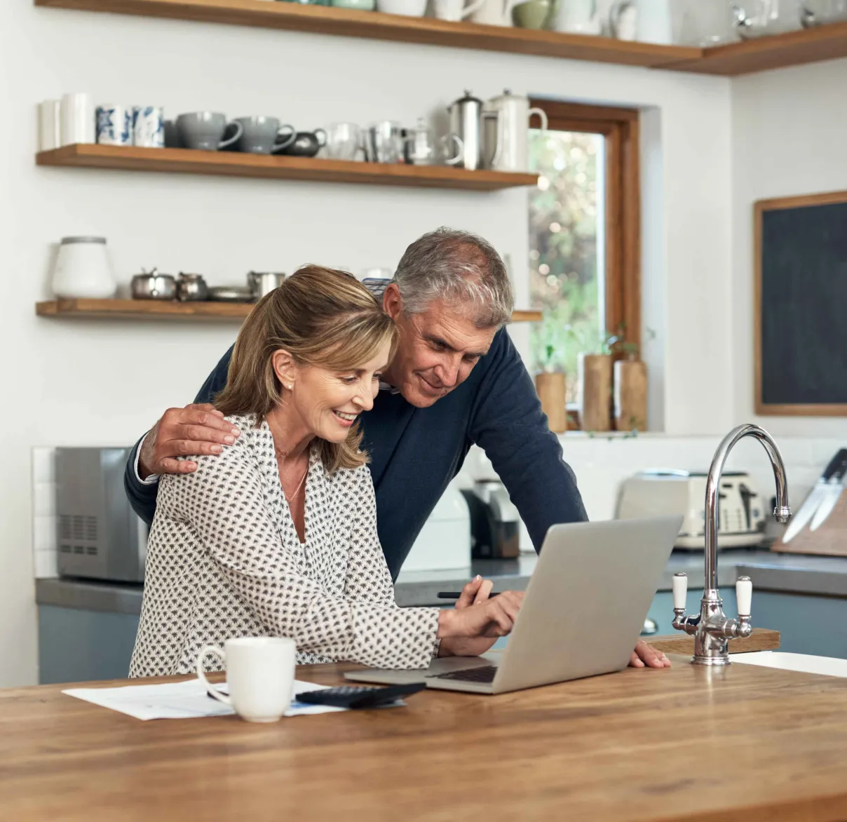 A couple sit at their kitchen table while looking at information on their laptop