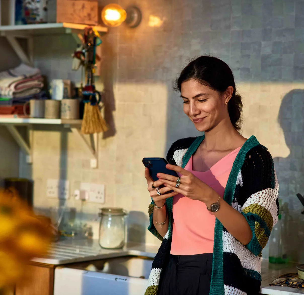 A lady leans against her kitchen sink while using her smartphone