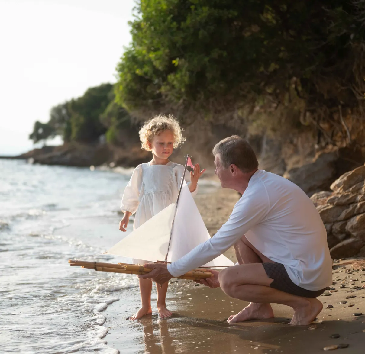 Father and daughter pushing toy boat into the ocean