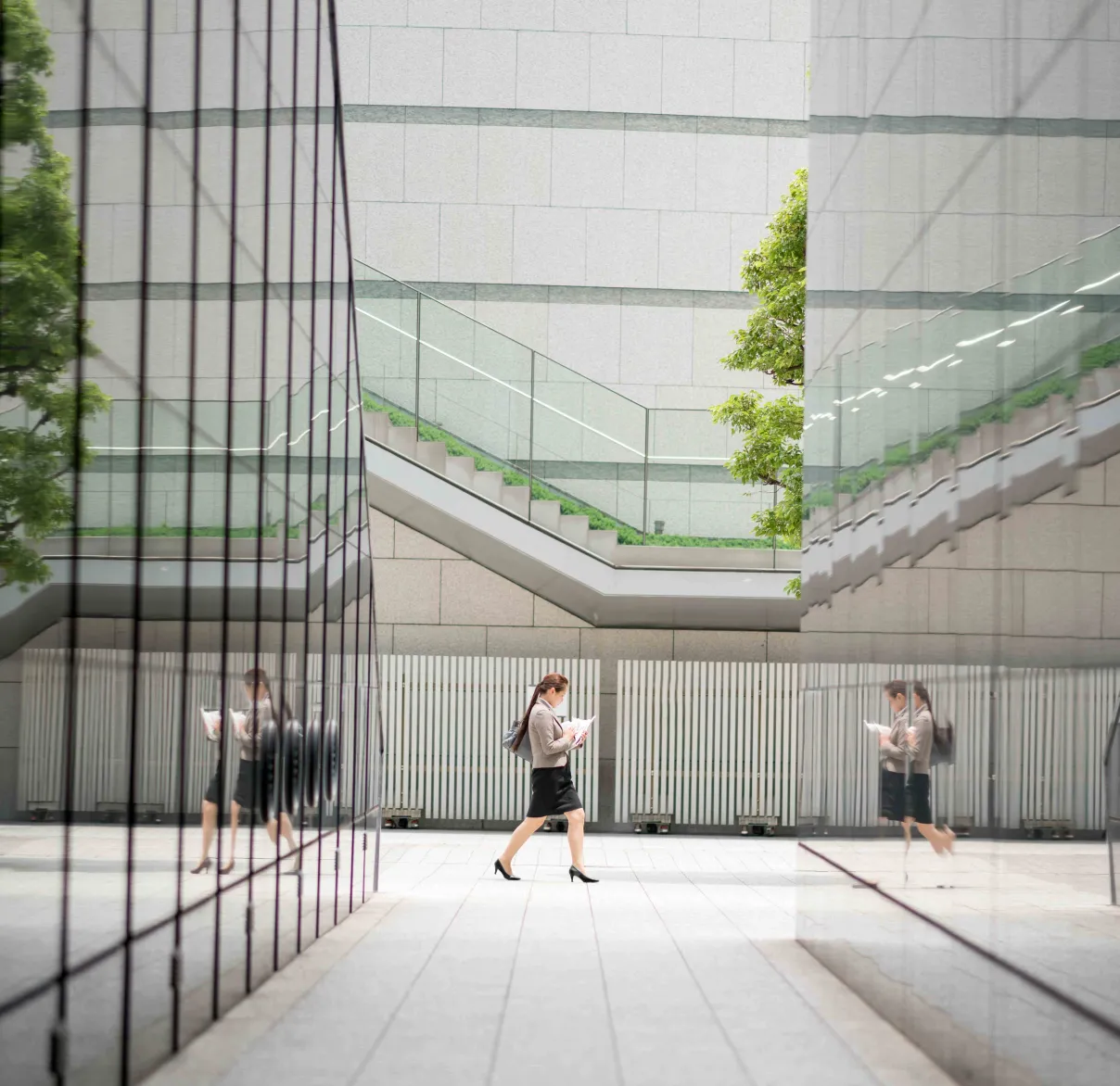 An office worker walks between buildings in the city, their figure reflected on the glass of the buildings around them