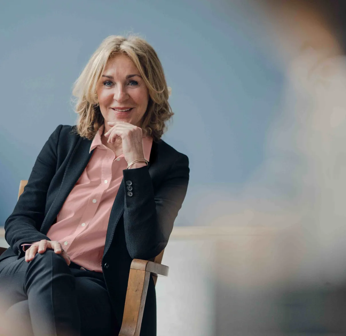 A businesswoman sits in a chair and looks confidently towards the camera