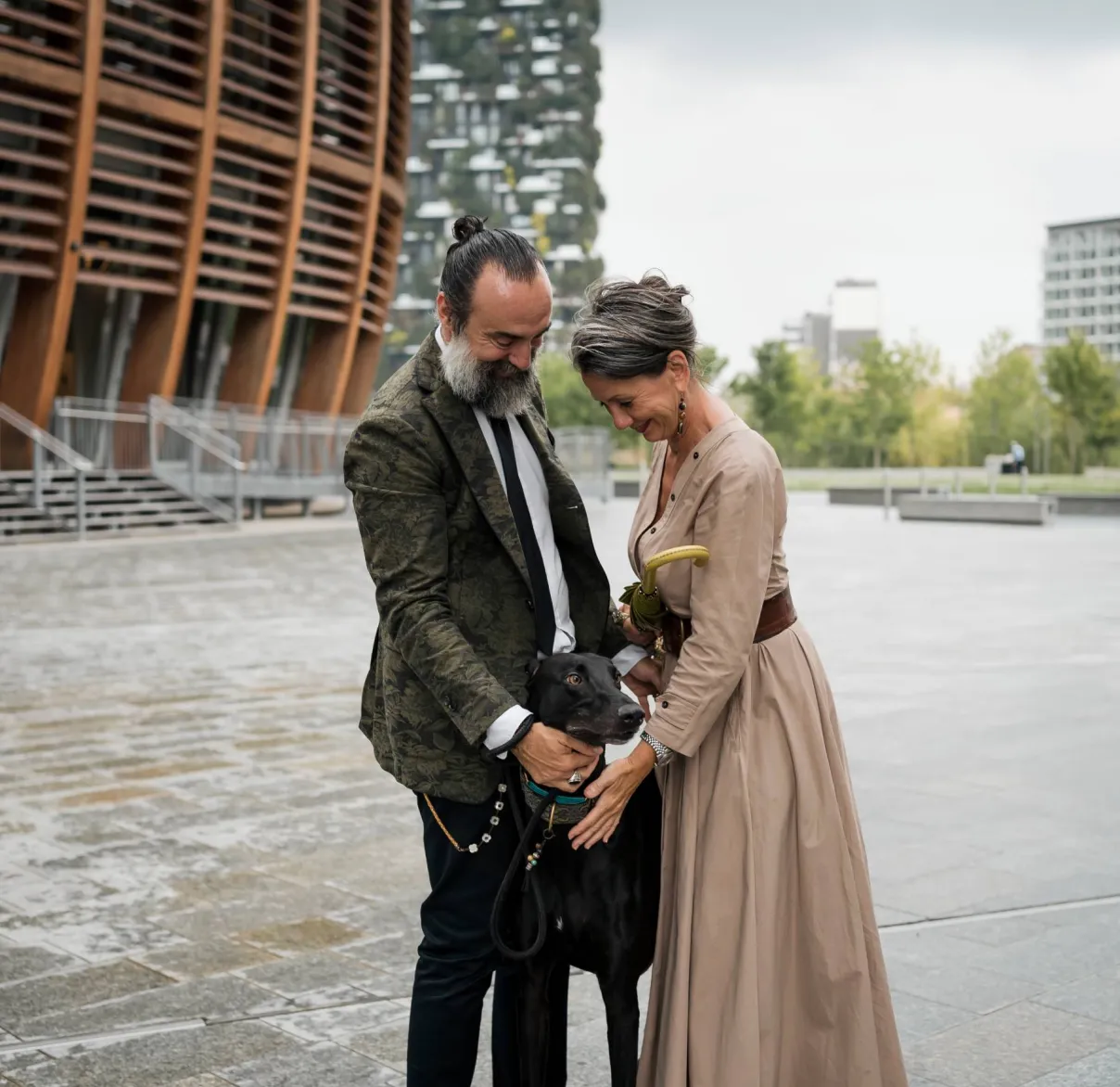 A couple stand together outdoors with their dog on a rainy day