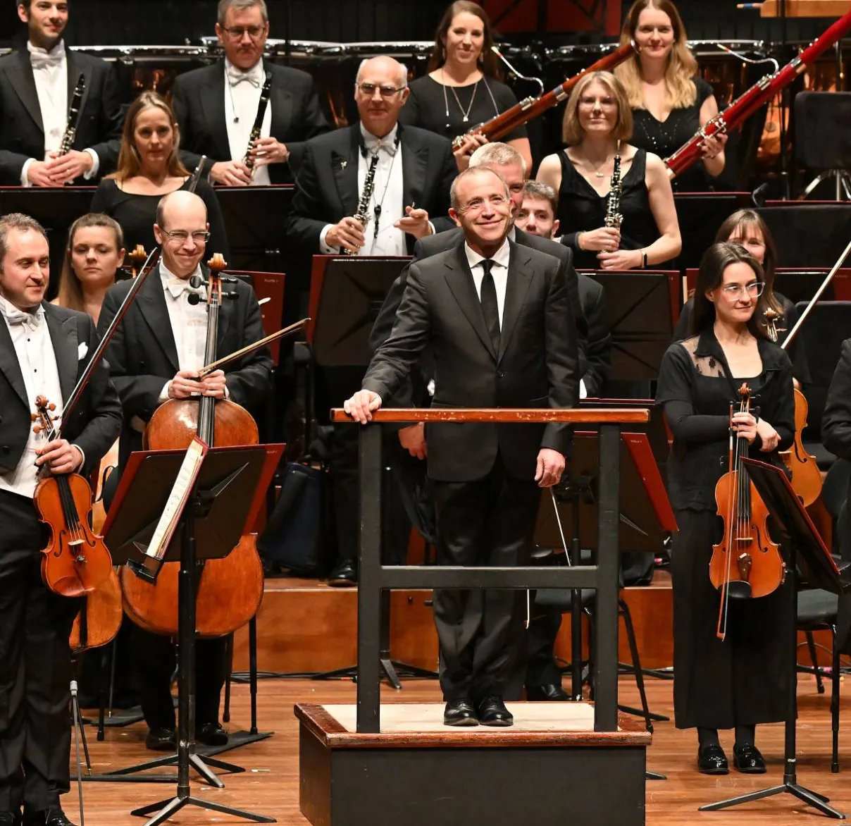 The Bournemouth Symphony Orchestra stands while the audience applauds, with conductor Mark Wigglesworth in front