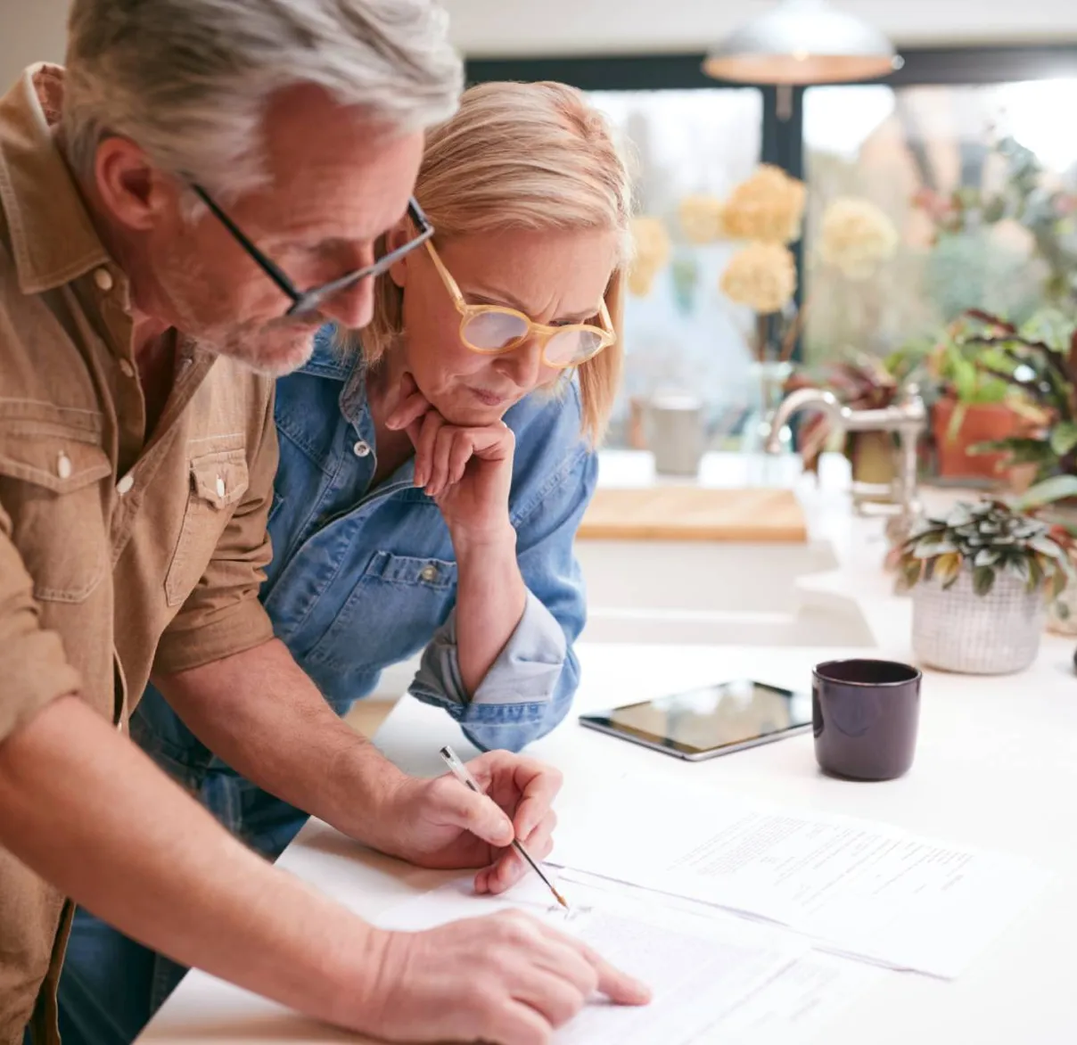 A couple look at paperwork spread out across their kitchen bench together