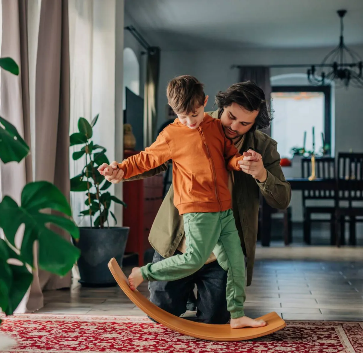 A man and son play together at home on a balance board