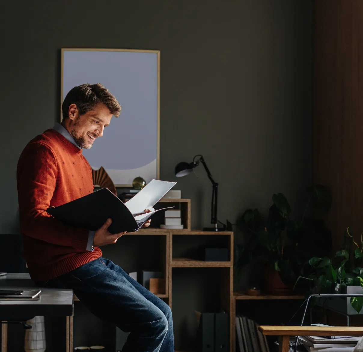 An entrepreneur leans against their desk in an office and reads documents