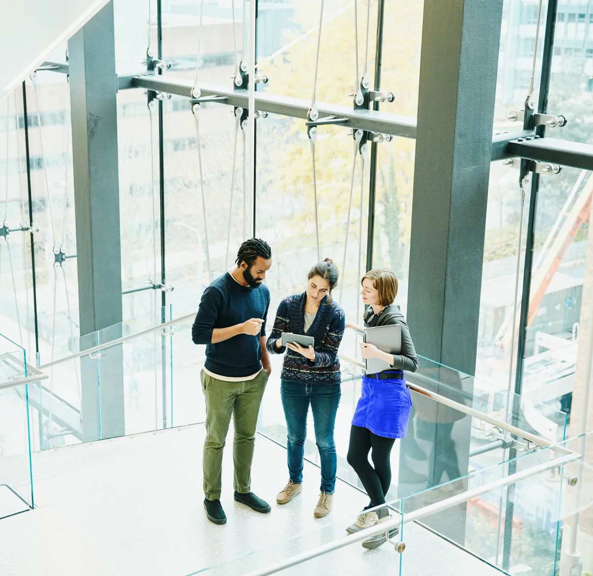 Thee office workers talk on the stairs of a glass corporate office building