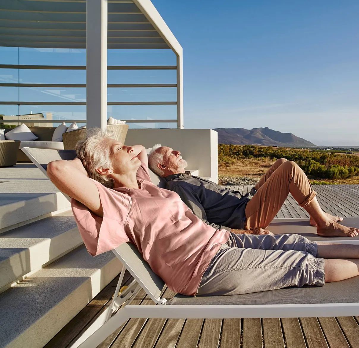A couple reclining on sun-beds on a decking over looking the sea.