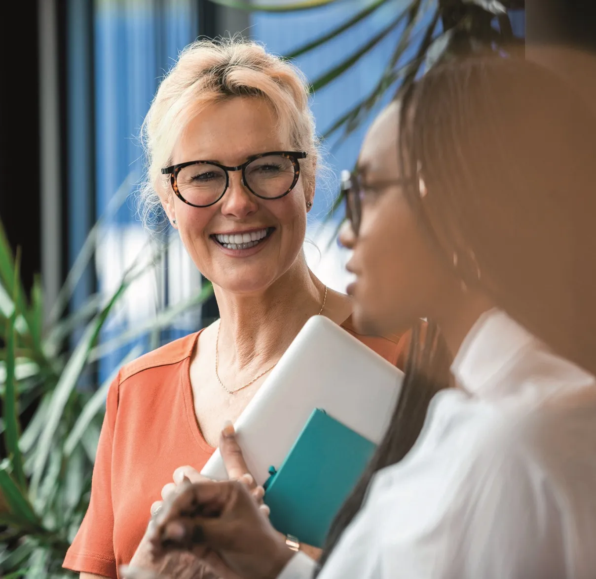 A lady with grey hair wearing black framed glasses, smiling at another lady wearing glasses