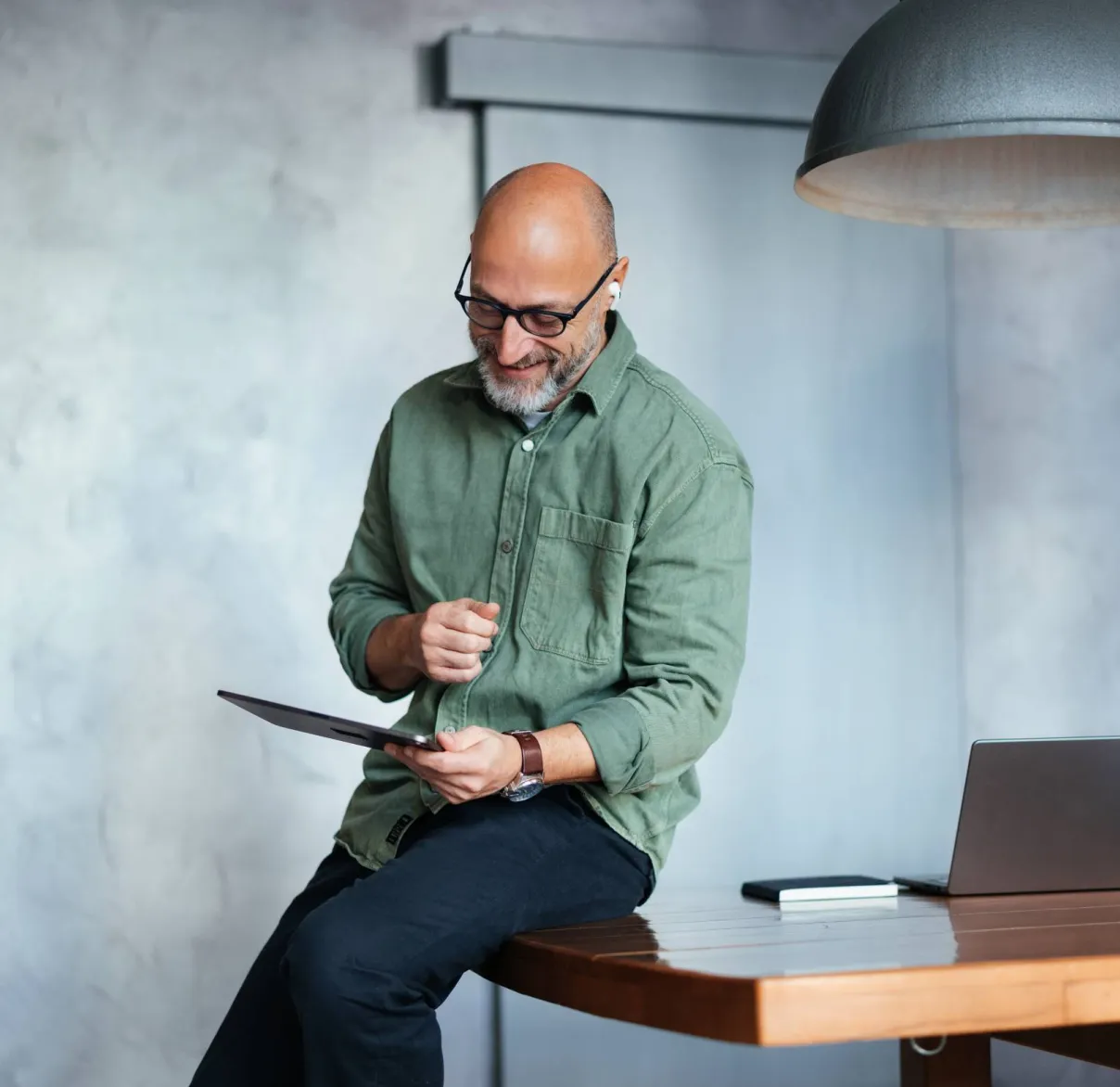 A man leans on his desk while looking at a tablet device