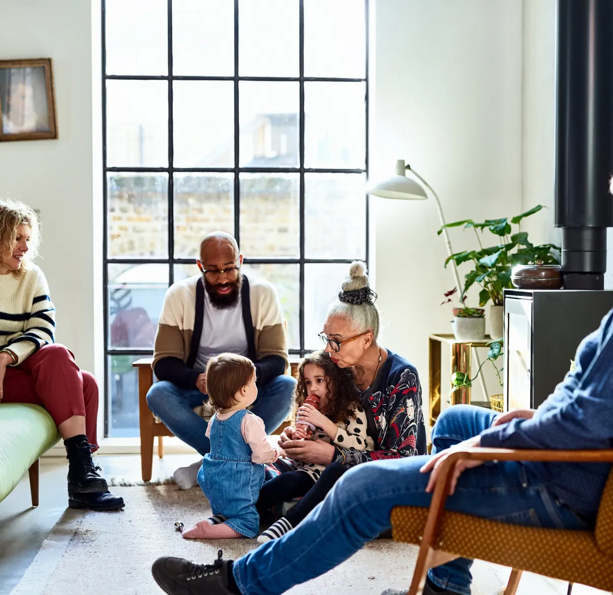 A family relax in their living room at home, with a grandmother playing with her grandchildren on the floor
