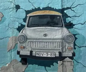 street art depicting a car breaking through a wall towards the viewer