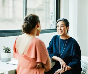 Two women talking together in a white-walled meeting space