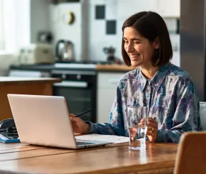 A woman talks on a video call on her laptop while sitting in her kitchen