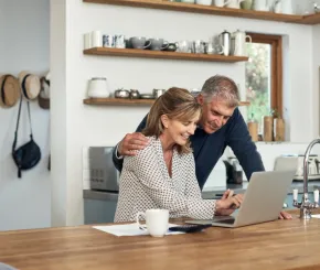 A picture of a couple in their kitchen looking at a laptop