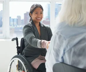 A confident businesswoman with a disability is sitting in a wheelchair and shaking hands with a colleague.