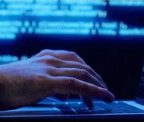 Fingers poised over a laptop keypad, with blue light in the background