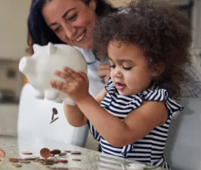 A child emptying her piggy bank as her mother watches