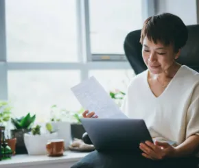 Older aisan lady looking at her tablet and documents sat by a window