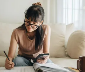 Young woman wearing glasses writing in a notepad on a coffee table