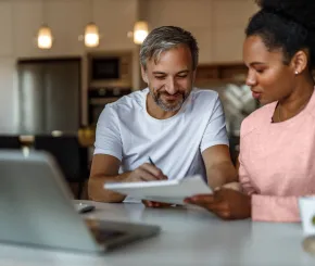 A couple draw on a document in front of a laptop in their home